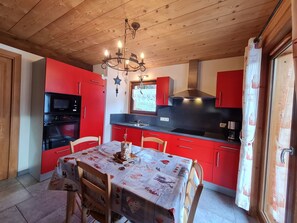 Uma cozinha compacta com armários vermelhos, fogão preto e mesa de jantar para quatro pessoas.