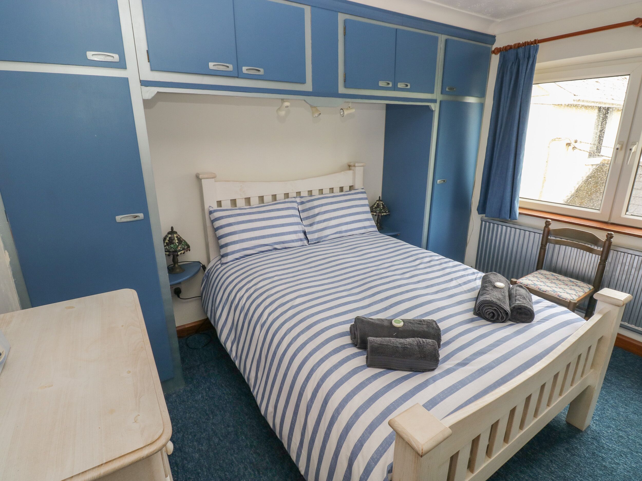 A bedroom with a bed, a chair, a nightstand, and a window with curtains.