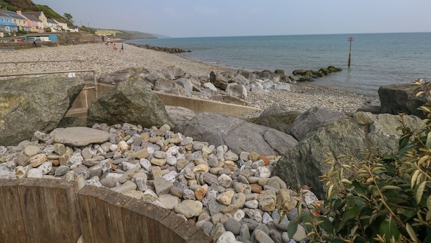 Een rotsachtig strand met een houten afscheiding, een heldere lucht en een rustige zee.