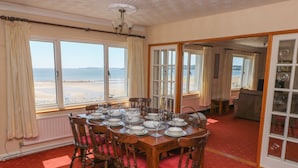 Een eetkamer met uitzicht op het strand, een rood tapijt, houten stoelen en een gedekte tafel voor zes personen.