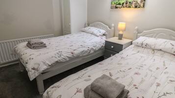 Quarto com duas camas de solteiro, uma mesa de cabeceira com abajur, um radiador e um quadro na parede.