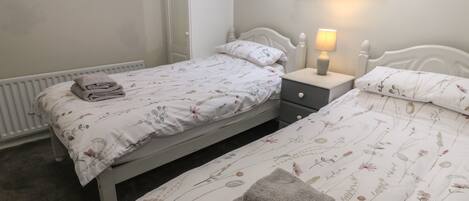A bedroom with two single beds, a bedside table with a lamp, a radiator, and a picture on the wall.