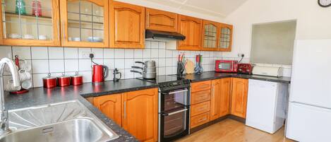 Eine Küche mit Holzausstattung, einer Edelstahlspüle, einer Mikrowelle, einem Toaster und einem Kühlschrank.