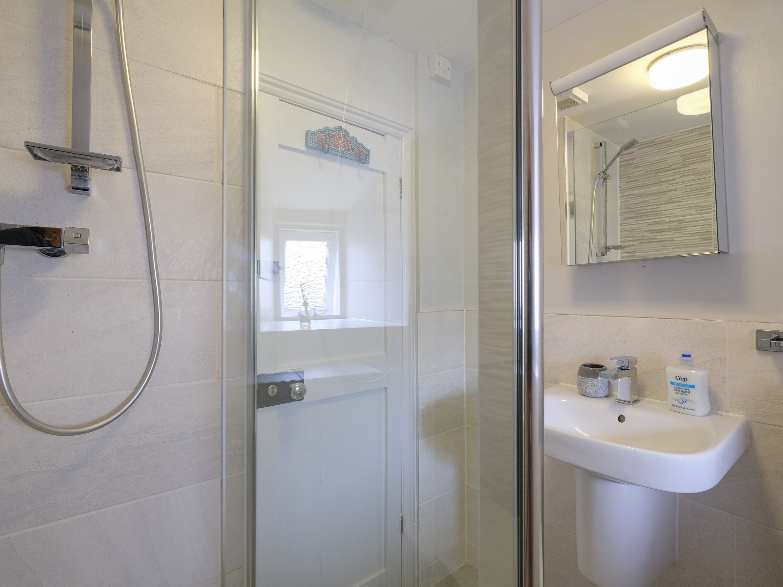 A modern bathroom with a glass shower enclosure, a white sink, and a mirror above it.