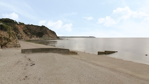 A beach with a rocky cliff, calm water, and a clear sky. - Lantern Cottage (St Austell)