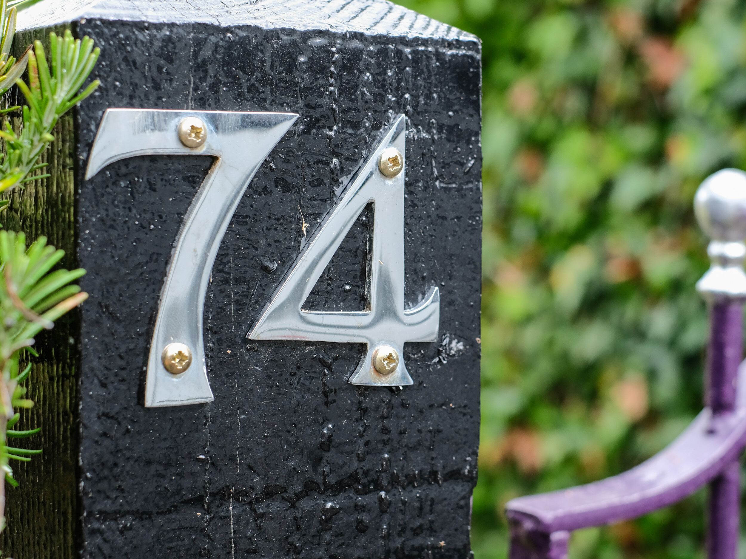 A house number '74' on a black, textured post with two screws.