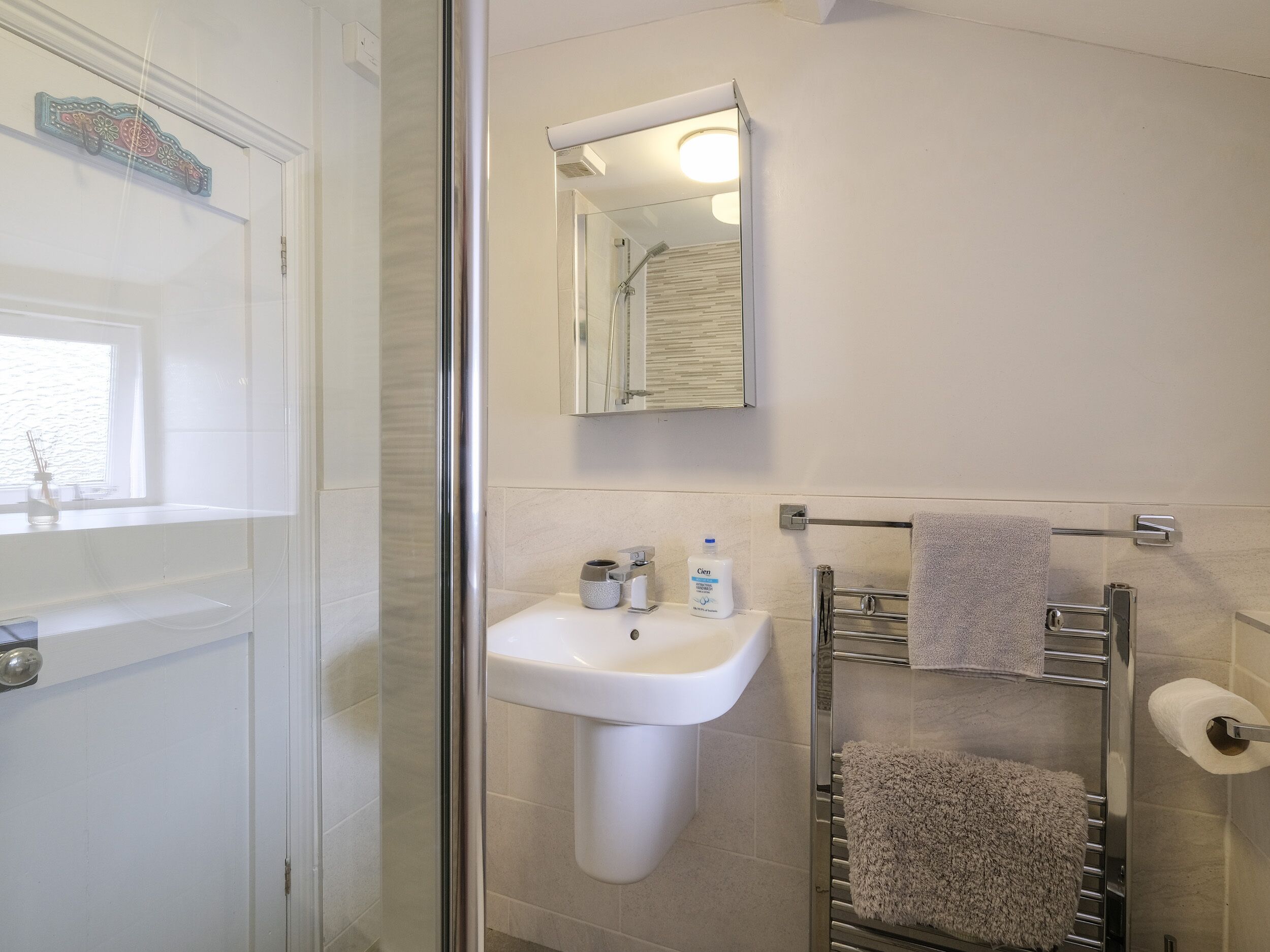 A bathroom with a glass shower enclosure, a white sink, a mirror, and a towel rack with towels.
