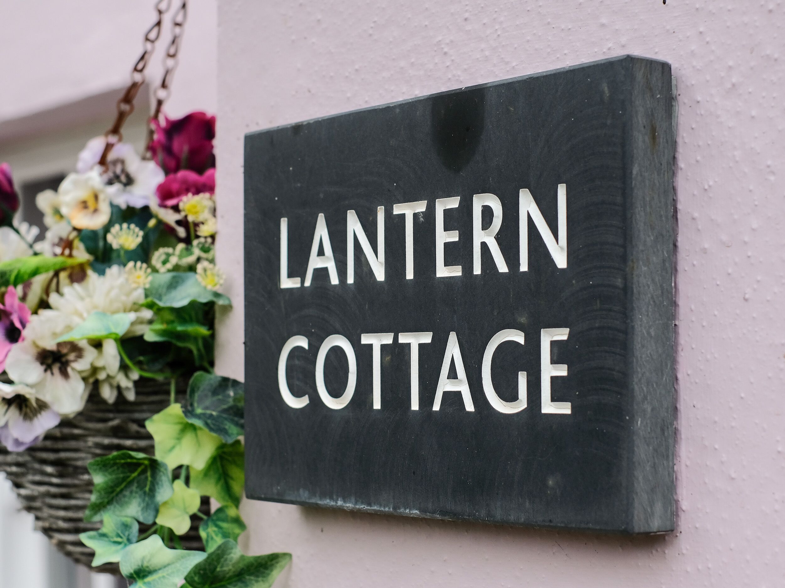 A black sign with white lettering that reads "LANTERN COTTAGE" mounted on a wall.