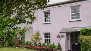 A pink cottage with a sign reading "Lantern Cottage," a stone pathway leading to the entrance, and a well-maintained garden with pink flowers. - Lantern Cottage (St Austell)