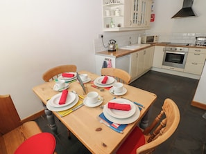 Un comedor con una mesa de madera dispuesta para cuatro personas, con platos, tazas y cubiertos.