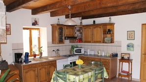 Una cocina con armarios de madera, una mesa de comedor con sillas, una estufa, un microondas y diversos utensilios de cocina.