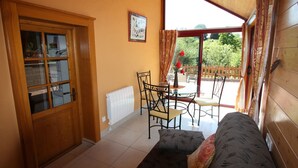 Una habitación acogedora con una puerta de madera, una mesa de vidrio con sillas, un sofá y vistas a un jardín a través de un ventanal grande.