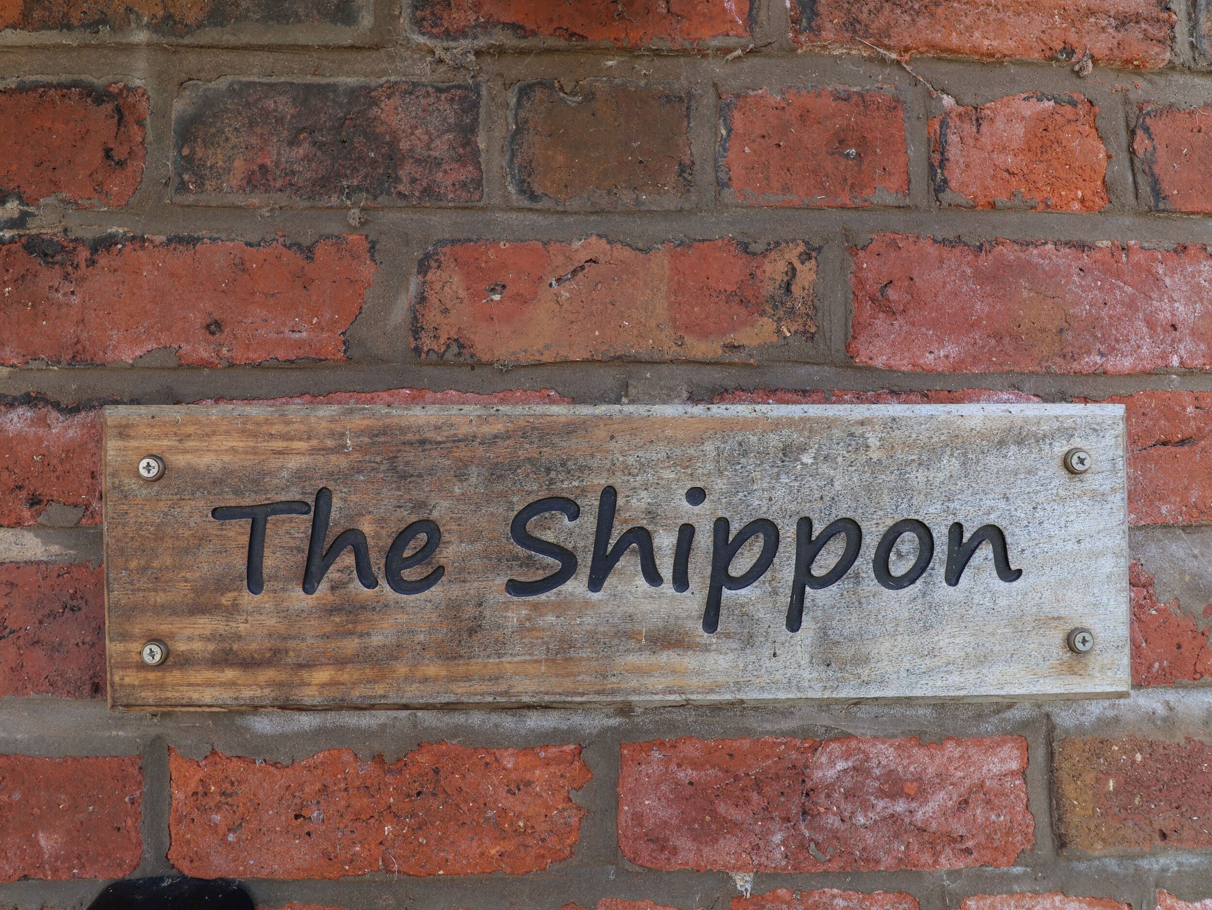A wooden sign with the text "The Shippon" mounted on a brick wall.