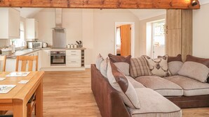 A cozy living room with a wooden ceiling, a sofa with patterned cushions, and a dining area with a wooden table and chairs. - The Shippon (Chester)
