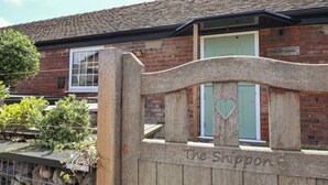 A wooden gate with "The Shippon" engraved on it, leading to a brick building with a green door and a window. - The Shippon (Chester)