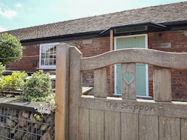 A wooden gate with "The Shippon" engraved on it, leading to a brick building with a green door and a window.