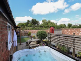 Un jacuzzi en un patio trasero con un muro de ladrillo, una terraza de madera y un quiosco telefónico rojo.