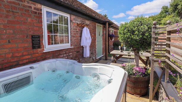 A brick building with a hot tub, a wooden table, and a green door. - The Shippon (Chester)