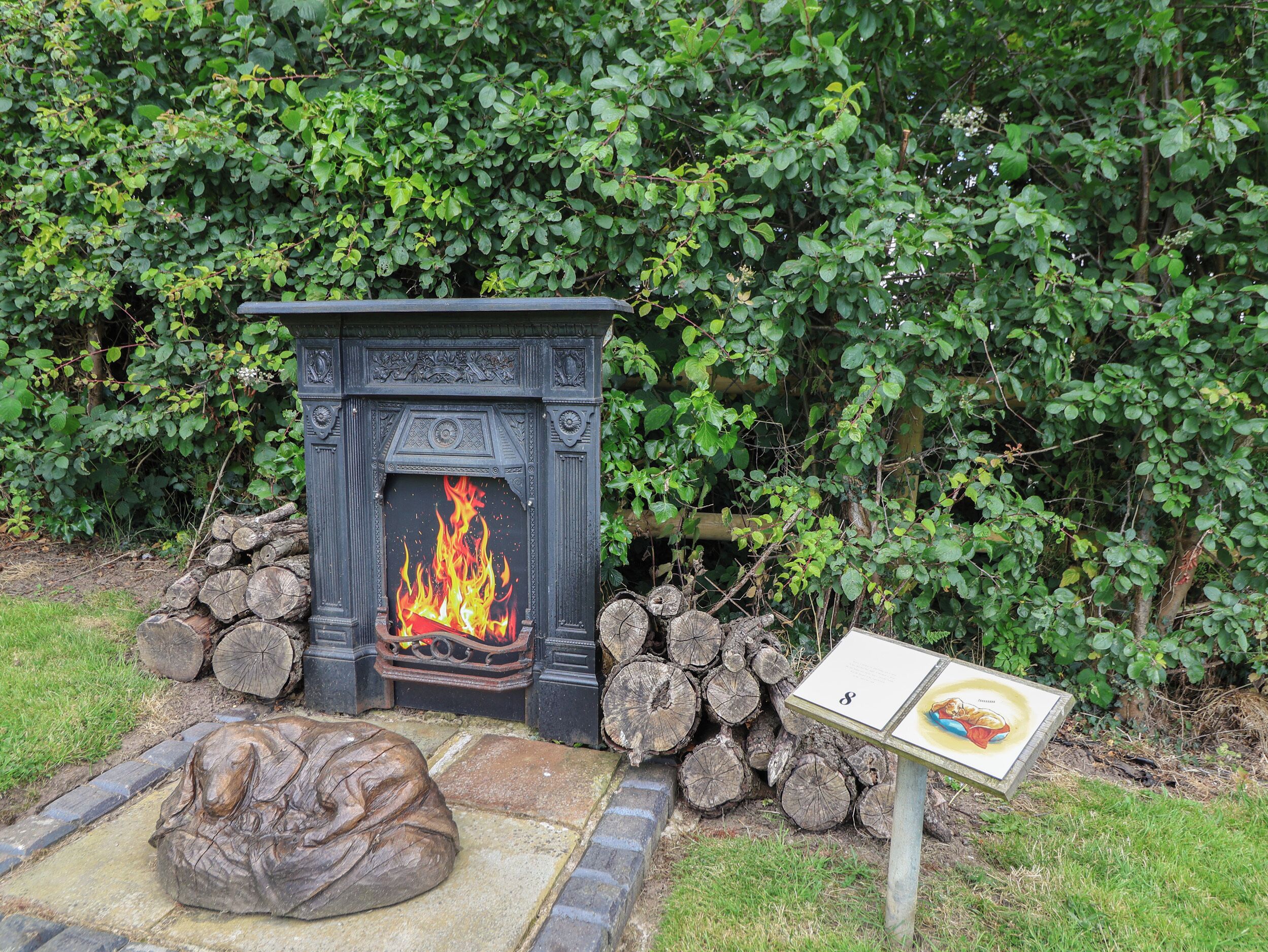 A fireplace with a fire, surrounded by logs and a stone bench.