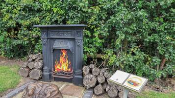 A fireplace with a fire, surrounded by logs and a stone bench.