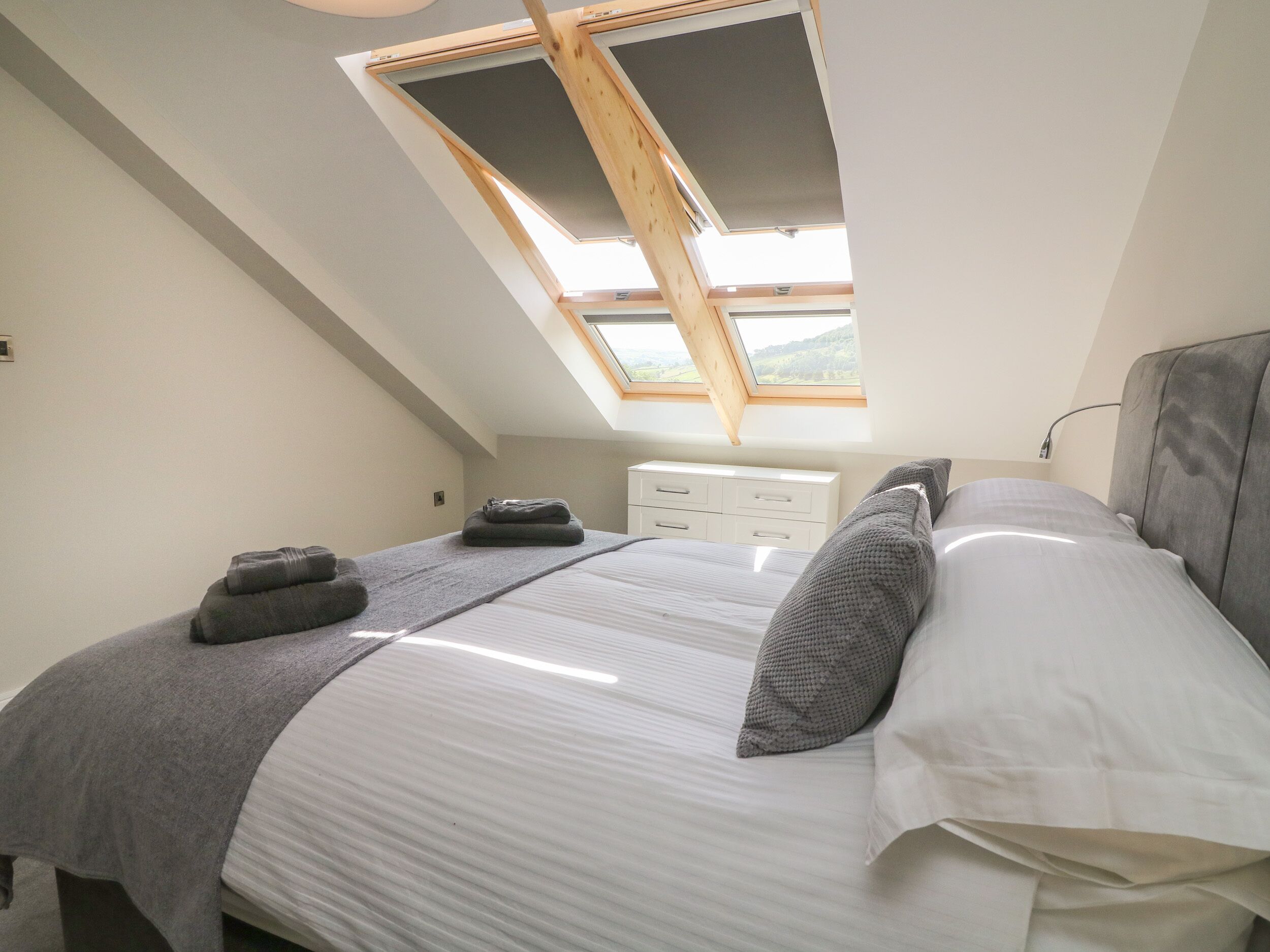 A bedroom with a skylight, a bed with pillows, a bedside table, and a dresser.