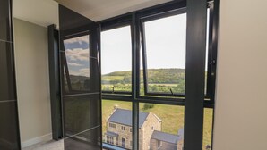 Ein Zimmer mit großen Fenstern und Blick auf eine ländliche Landschaft sowie ein Steinhaus.