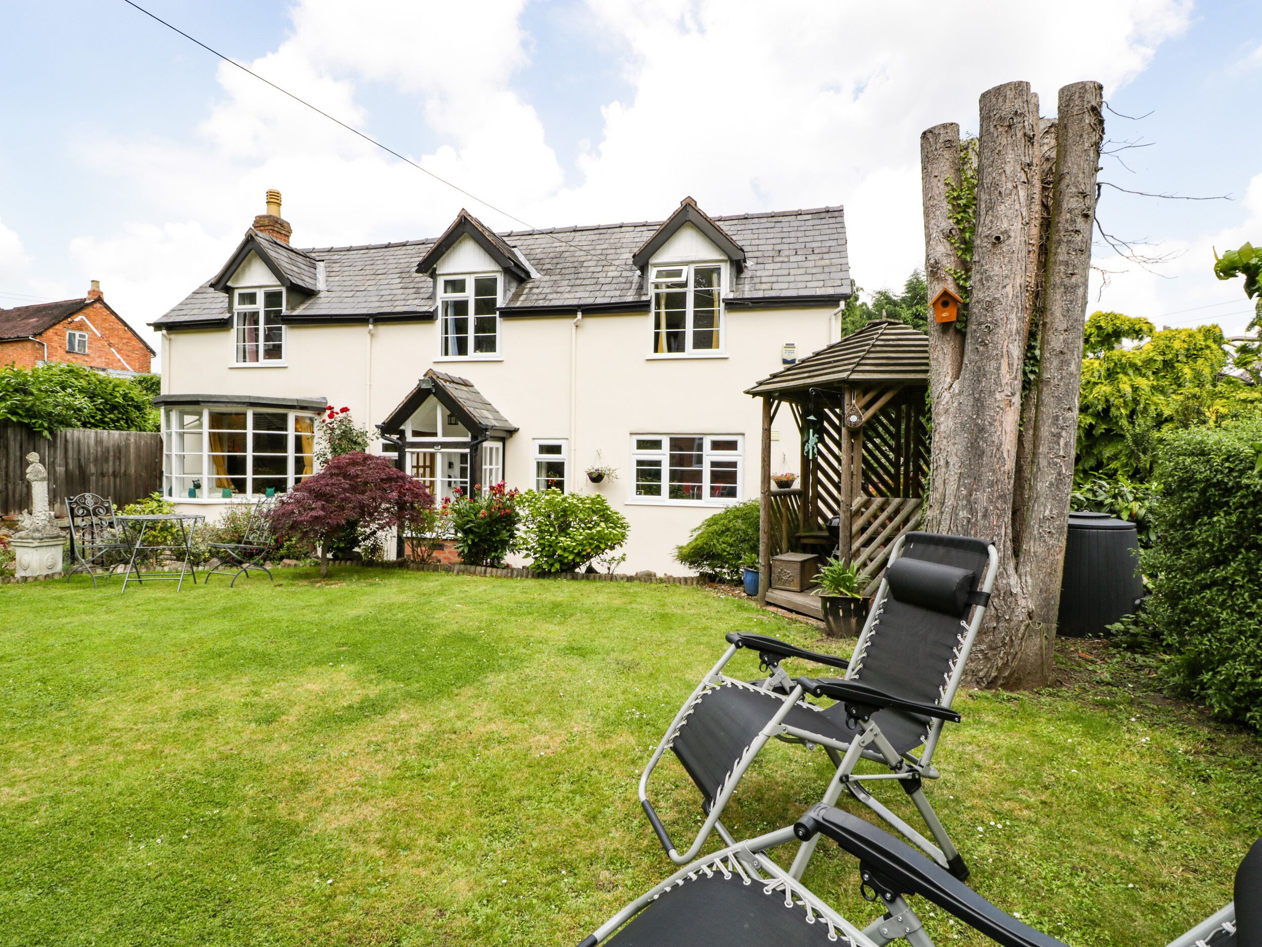 A two-story house with a garden, a gazebo, and a tree.