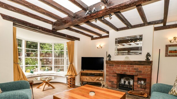 A cozy living room with a wooden coffee table, two teal sofas, a TV, and a fireplace. - Eleri Cottage (Malvern)