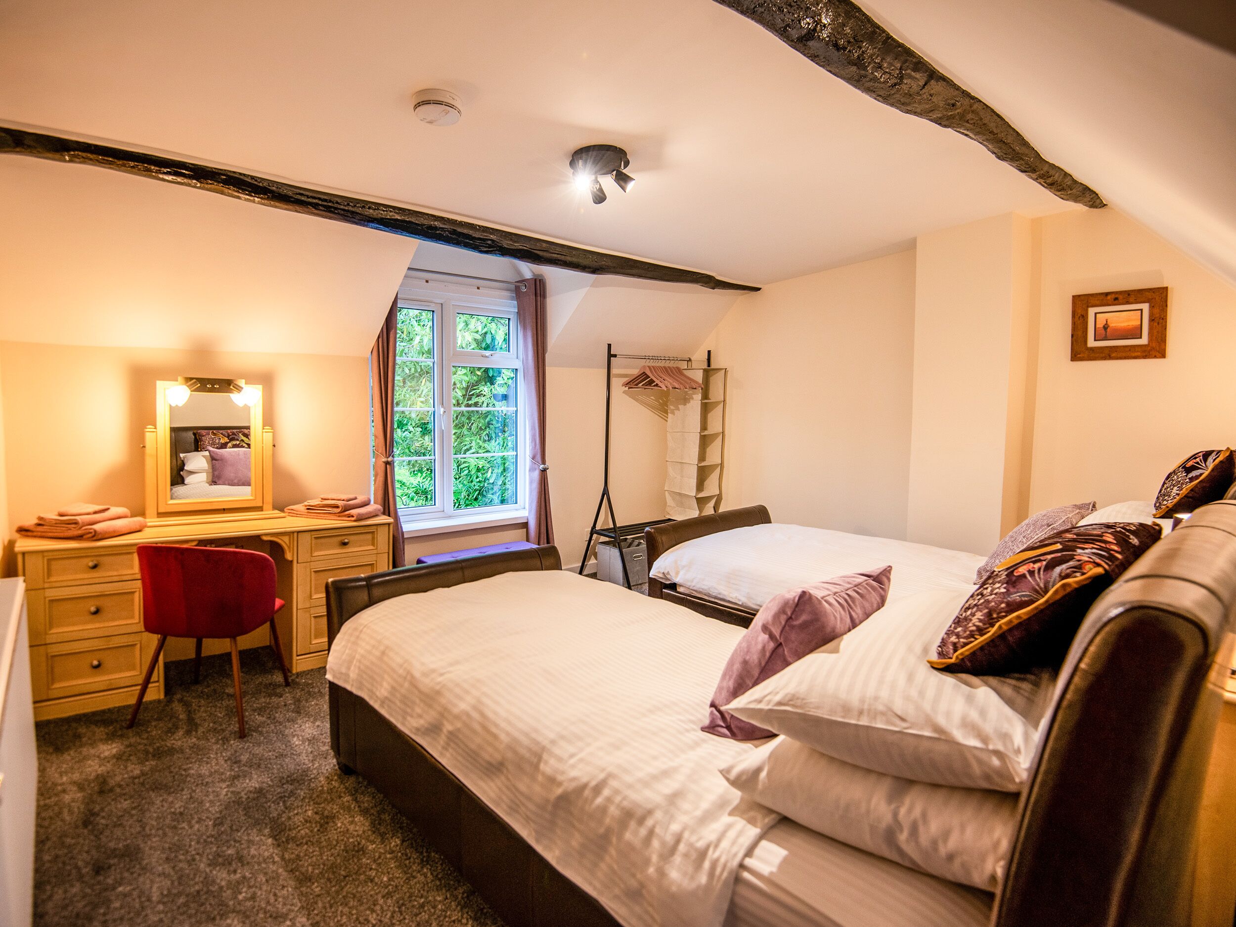 A bedroom with two beds, a desk, a chair, a mirror, a window with curtains, and a ladder.
