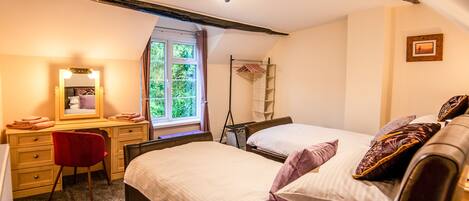 A bedroom with two beds, a desk, a chair, a mirror, a window with curtains, and a ladder.