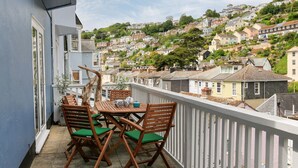 En balkong med ett träbord och stolar, med utsikt över ett bostadsområde som ligger på en sluttning.