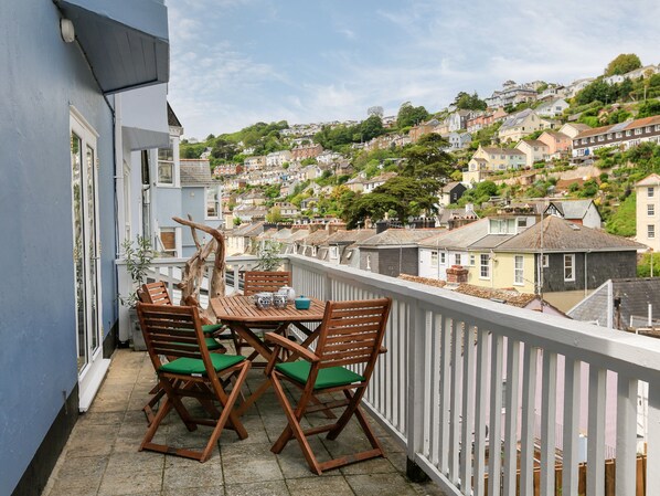 A balcony with a wooden table and chairs, overlooking a hillside residential area.