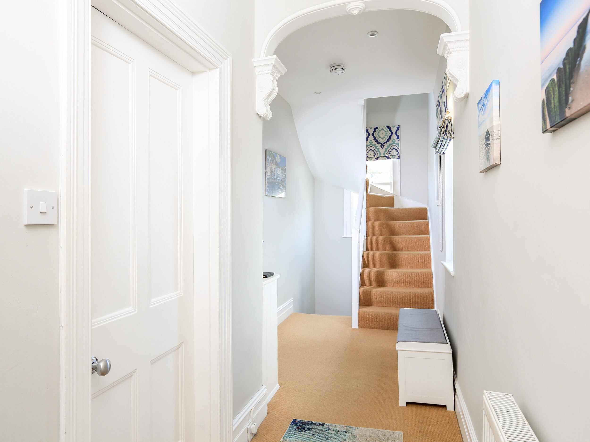 A hallway with a white door, a carpeted staircase, and a small white table.
