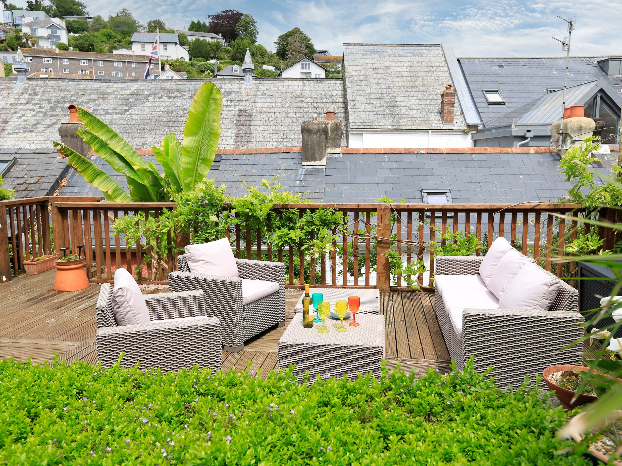 A rooftop patio with wicker furniture, potted plants, and a view of the surrounding neighborhood.