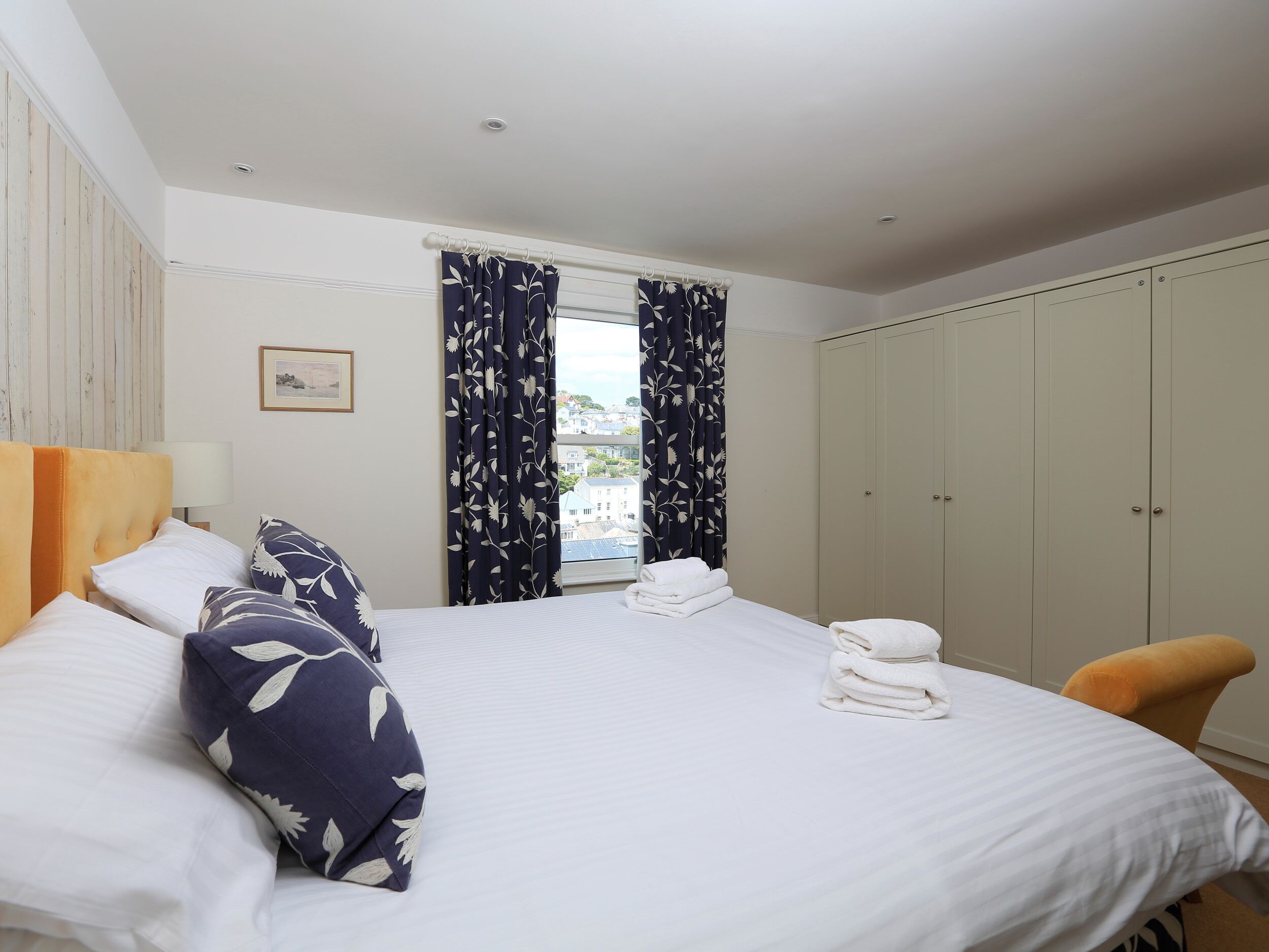 A hotel room with a bed, a chair, a wardrobe, and a window with curtains.