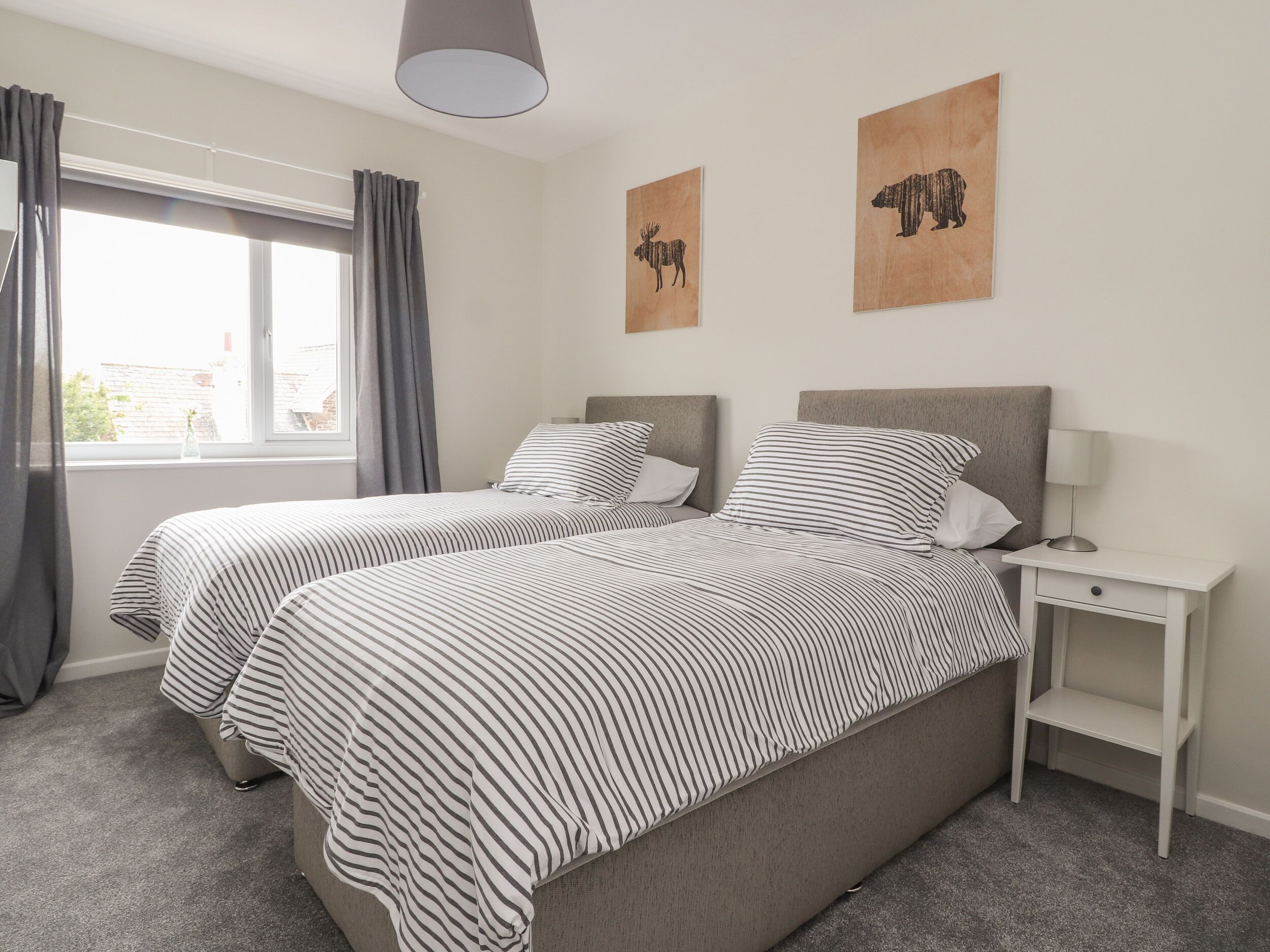 A double bed with striped bedding, a bedside table with a lamp, and two wall art pieces depicting animals.