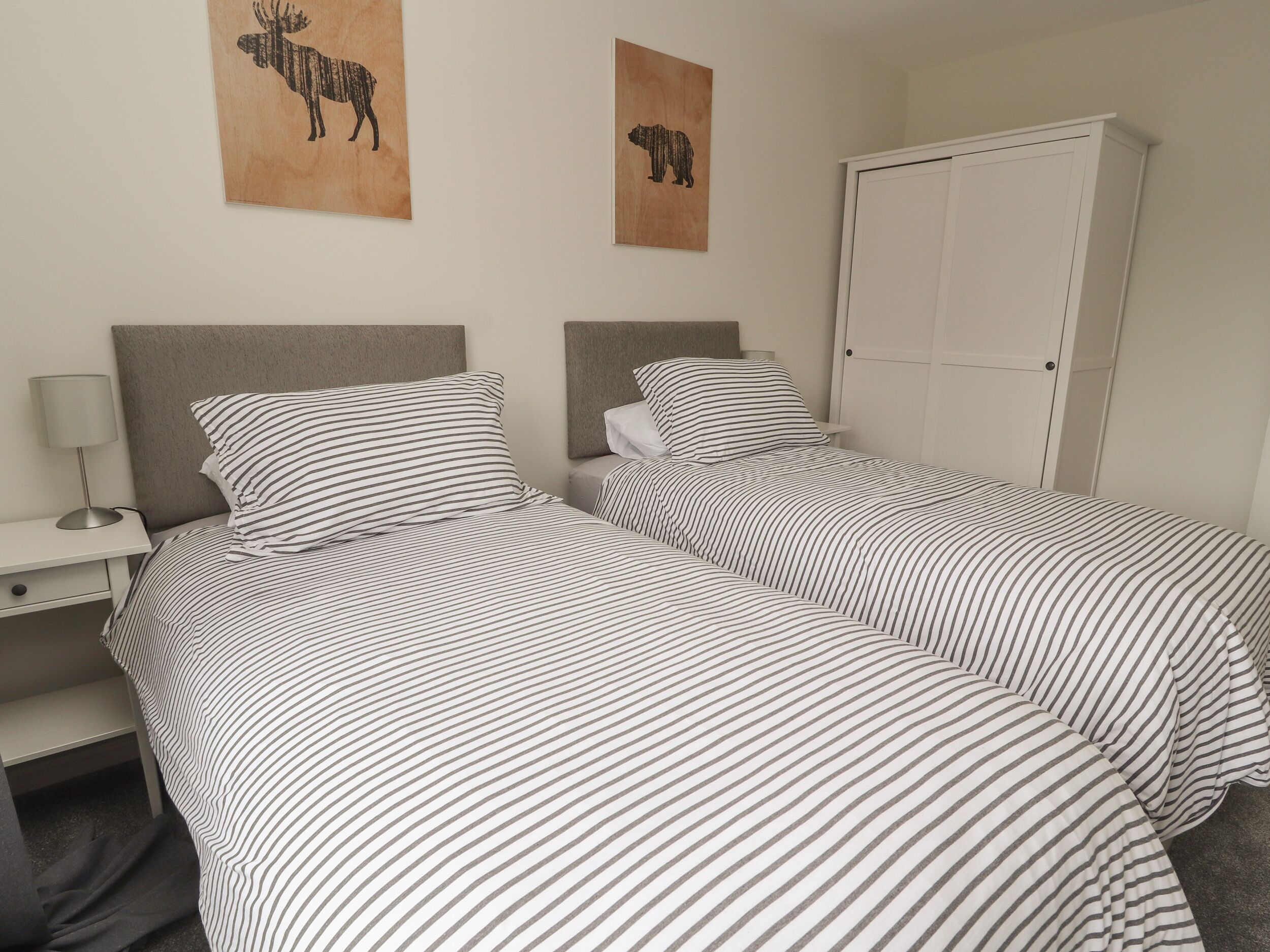 A twin room with two beds, a nightstand, a lamp, and a wardrobe.