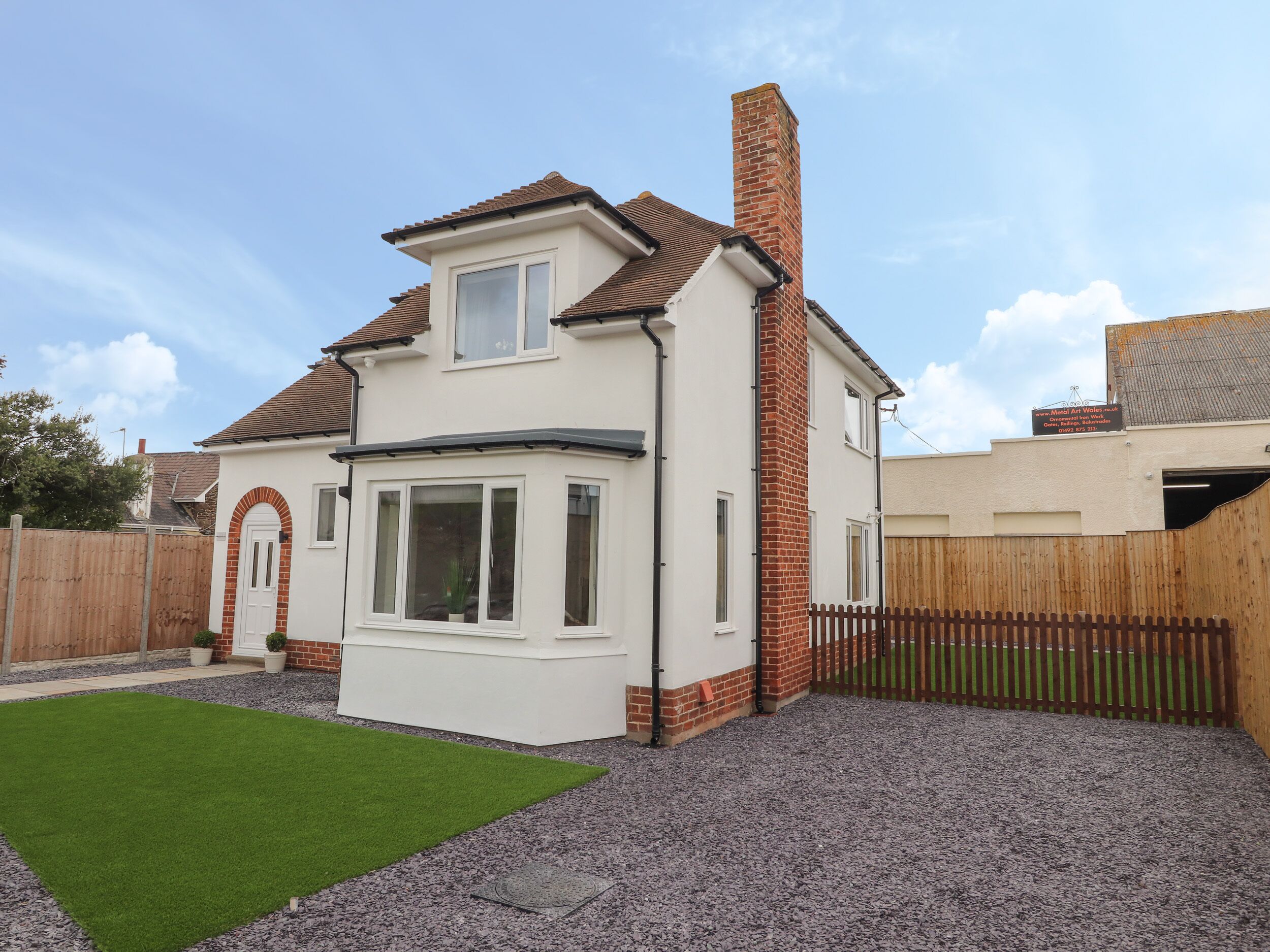 A two-story house with a brick chimney, a white exterior, and a small front yard with artificial grass.