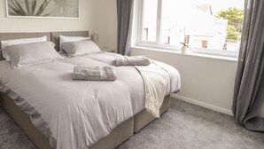 A neatly made bed with pillows and a blanket, a bedside table with a lamp, and a window with curtains.
