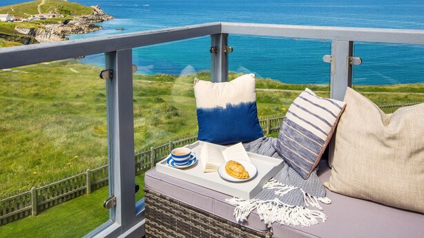 A balcony with a view of the sea, a wicker chair, a cushion, a plate with food, and a cup. - Breakers (Newquay)