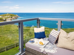 A balcony with a view of the sea, a wicker chair, a cushion, a plate with food, and a cup. - Breakers (Newquay)