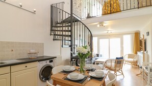 A modern kitchen with a built-in washing machine, a dining area with a table set for four, and a spiral staircase leading to an upper level. - Breakers (Newquay)