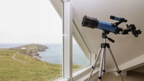 A telescope on a tripod by a window overlooking a coastal landscape. - Breakers (Newquay)