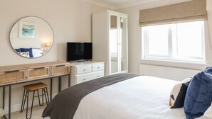 A bedroom with a bed, a TV, a desk with a chair, a wardrobe, and a window with curtains. - Breakers (Newquay)