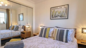 A hotel room with a large bed, a bedside table, a nightstand, a mirror, and a painting on the wall. - 5 Styleman Road (Hunstanton)