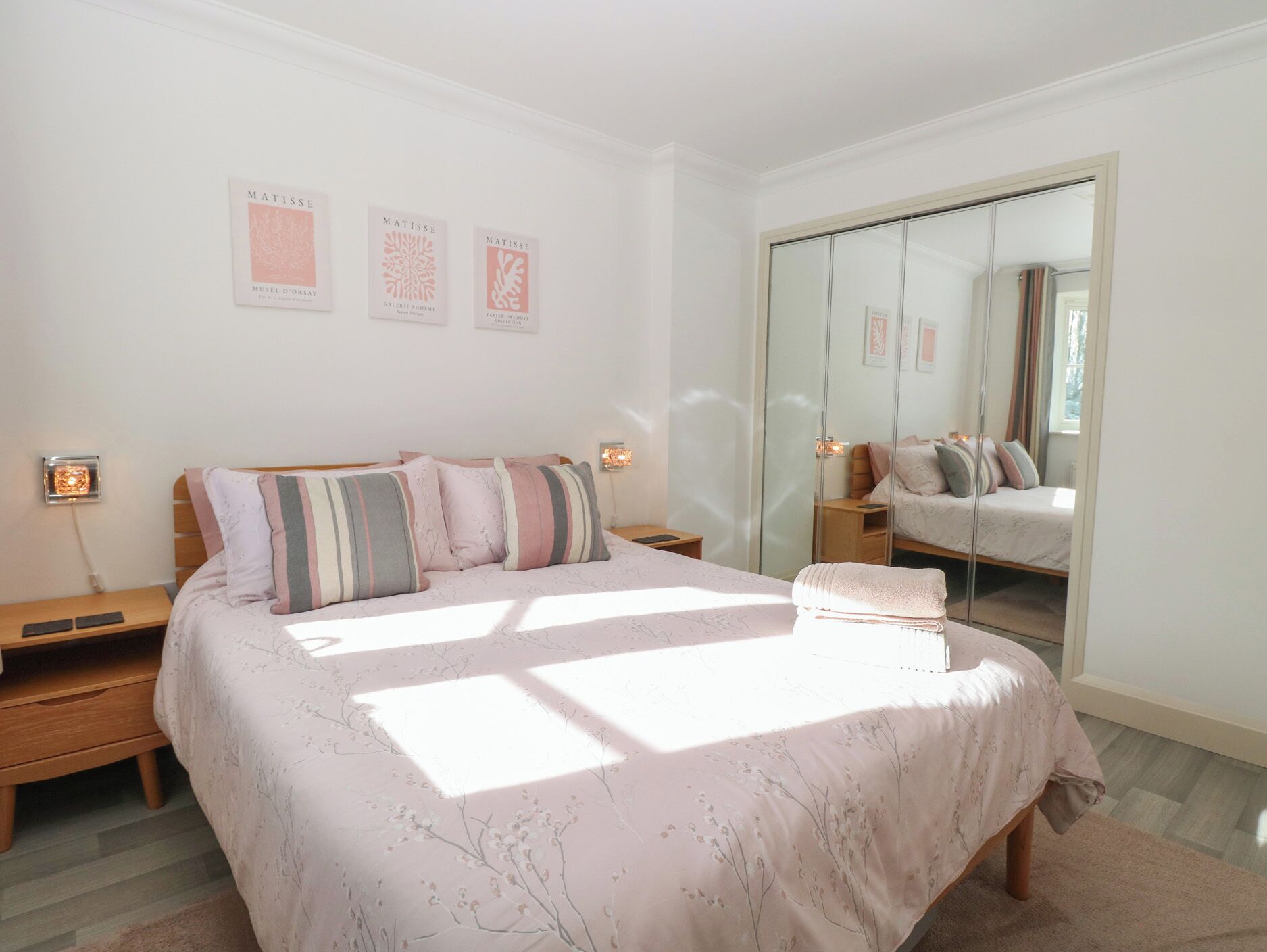 A bedroom with a large bed, bedside tables, a mirror, and artwork on the wall.