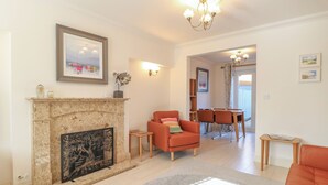 A living room with a fireplace, a sofa, a dining table with chairs, and a chandelier. - 5 Styleman Road (Hunstanton)