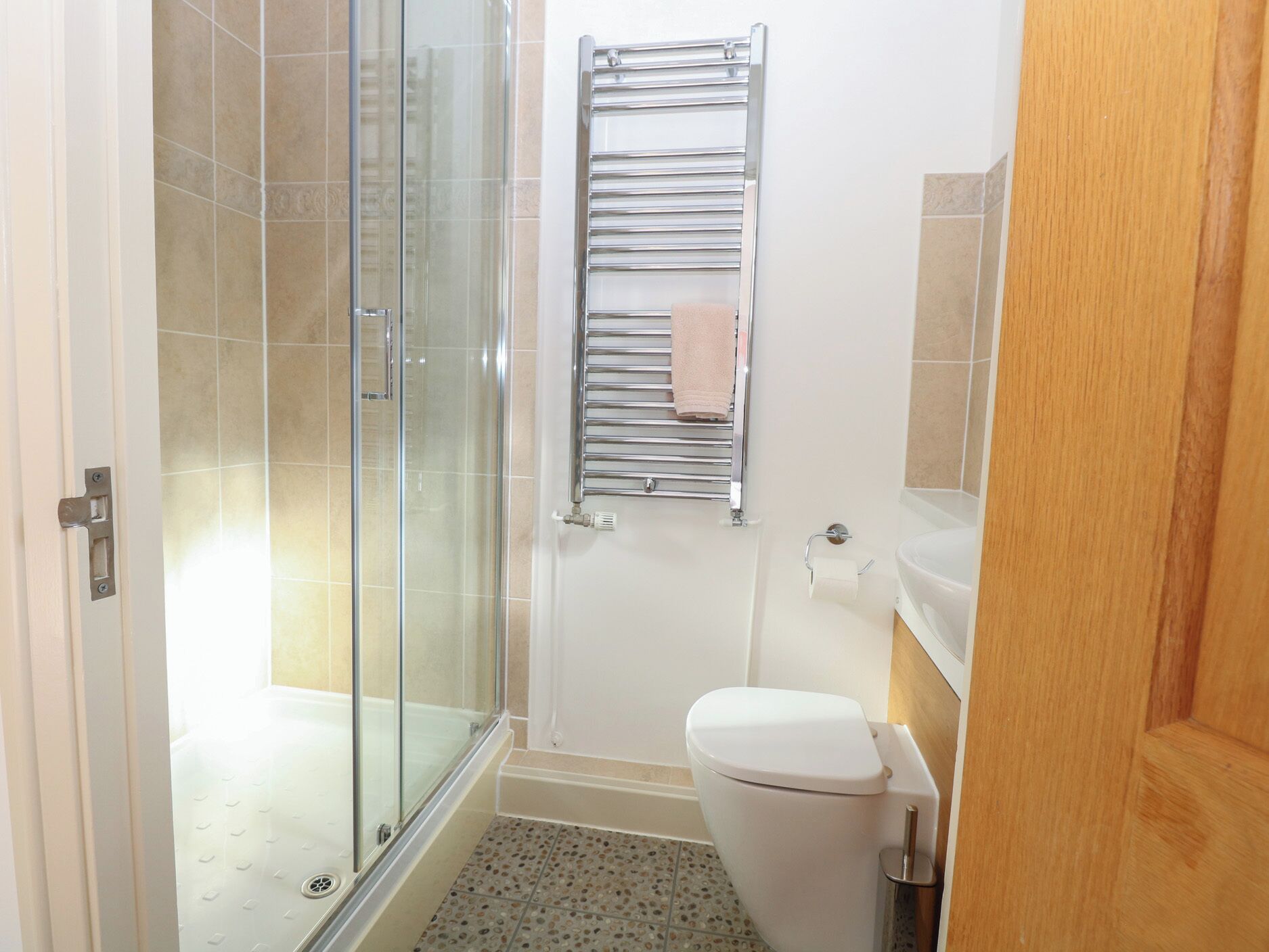A bathroom with a glass shower enclosure, a white toilet, and a towel rack with a pink towel.