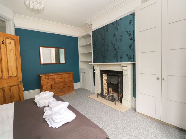 A bedroom with a bed, a dresser, a mirror, a fireplace, and a wardrobe.
