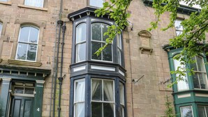A corner bay window with white curtains, a green door, and a stone building facade. - Belvedere (Buxton)